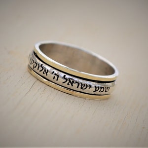 May include: A silver and gold spinning ring with Hebrew text that reads "Shema Yisrael Adonai Eloheinu Adonai Echad" which translates to "Hear O Israel, the Lord our God, the Lord is One".