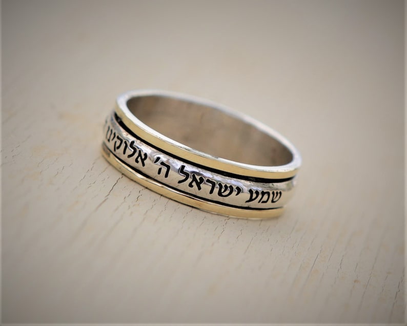 May include: A silver and gold spinning ring with Hebrew text that reads "Shema Yisrael Adonai Eloheinu Adonai Echad" which translates to "Hear O Israel, the Lord our God, the Lord is One".