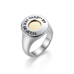 Peut inclure: Bague en argent avec un dessus circulaire avec un centre doré et du texte hébreu gravé. La bague a une finition lisse et polie et un style chevalière classique. La bague est un bijou.