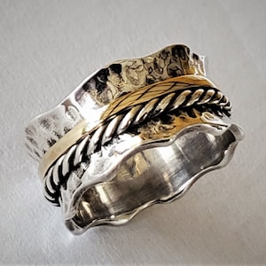 Puede incluir: Un anillo giratorio de plata y oro con una banda texturizada y un diseño de cuerda. El anillo está hecho de dos metales, plata y oro, y tiene una banda texturizada con un diseño de cuerda.
