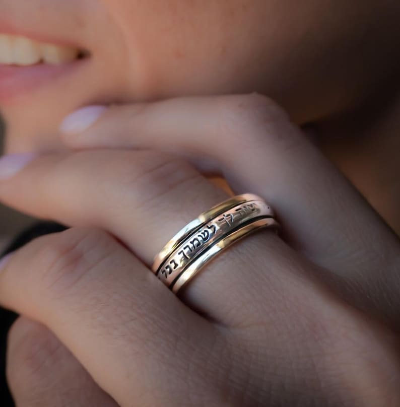 May include: A silver and gold spinning ring with Hebrew text inscribed on the band.