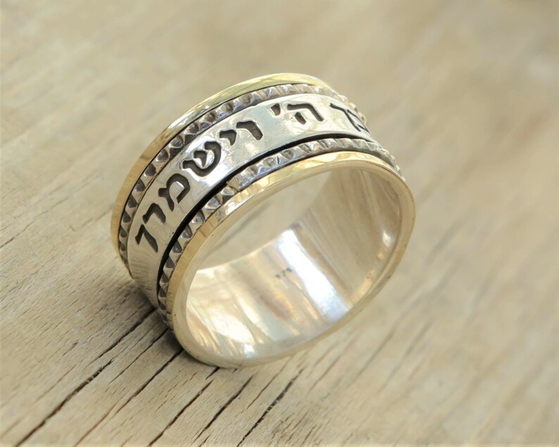 May include: A silver spinning ring with a gold band and Hebrew text. The text reads "לֹא תִירָא" which translates to "Do not be afraid".