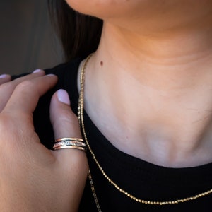 May include: A silver spinning ring with a textured design. The ring is worn on the index finger of a person wearing a black shirt.