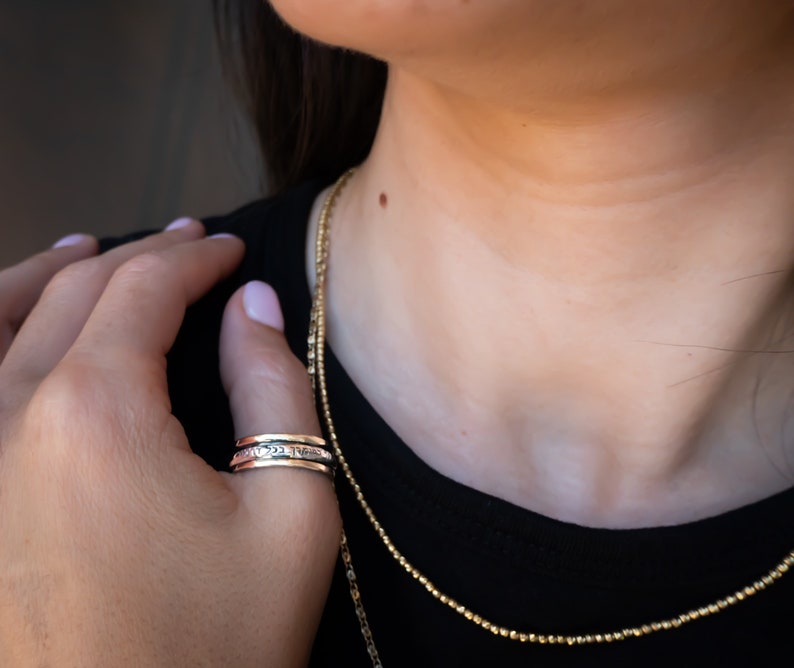 May include: A silver spinning ring with a textured design. The ring is worn on the index finger of a person wearing a black shirt.