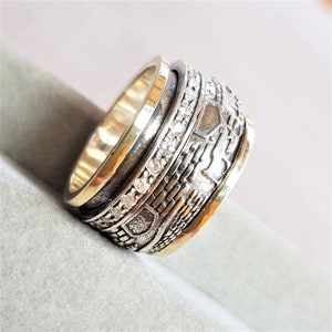 Puede incluir: Un anillo giratorio de plata y oro con un diseño texturizado y piedras transparentes. El anillo está hecho de múltiples bandas que giran independientemente.