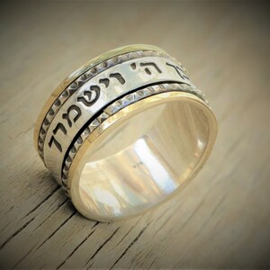 May include: A silver and gold spinning ring with Hebrew text inscribed on the band. The ring has a textured edge.