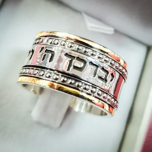 May include: A silver and gold ring with a Hebrew inscription. The inscription reads "Mah Tov U Mah Naim".
