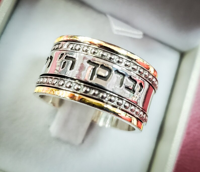 May include: A silver and gold ring with a Hebrew inscription. The inscription reads "Mah Tov U Mah Naim".