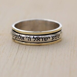 May include: A silver and gold spinning ring with Hebrew text that reads "Shema Yisrael Adonai Eloheinu Adonai Echad" which translates to "Hear O Israel, the Lord our God, the Lord is One".