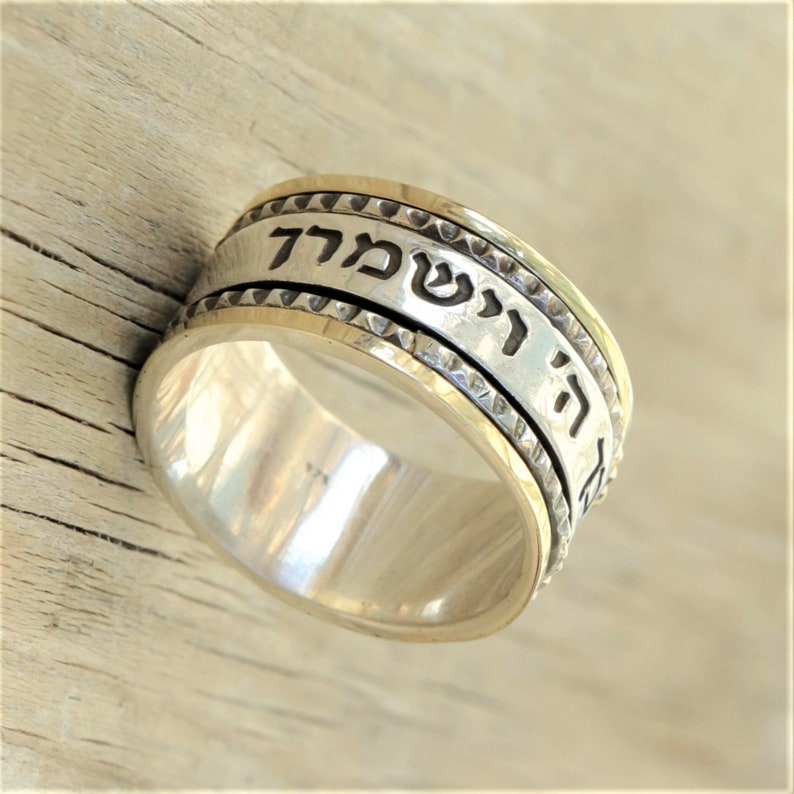 May include: A silver and gold spinning ring with Hebrew text that reads "Ha Shem" which means "The Name".