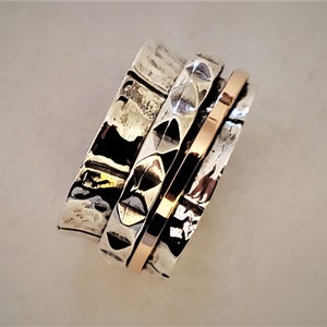 Puede incluir: Un anillo giratorio de plata y oro con una banda texturizada y un diseño geométrico. El anillo está hecho de tres bandas que giran independientemente.