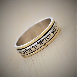 May include: A silver and gold spinning ring with Hebrew text inscribed on the band. The text reads "Shema Yisrael Adonai Eloheinu Adonai Echad" which translates to "Hear O Israel, the Lord our God, the Lord is One."