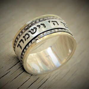May include: A silver and gold spinning ring with Hebrew text inscribed on the band. The text reads "Zeh Eli V'Ani Lo Yira"