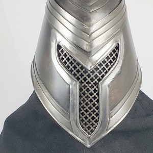 May include: A silver metal helmet with a mesh face mask and a raised design on the top. The helmet is on a black surface with a white label that says "CARAPAX".