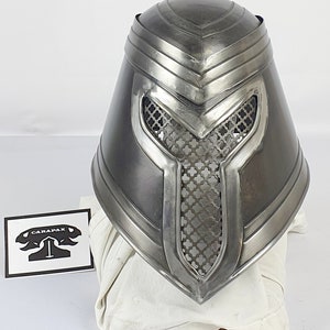 May include: A silver helmet with a mesh faceplate and a pointed top. The helmet has a decorative design on the top and sides.