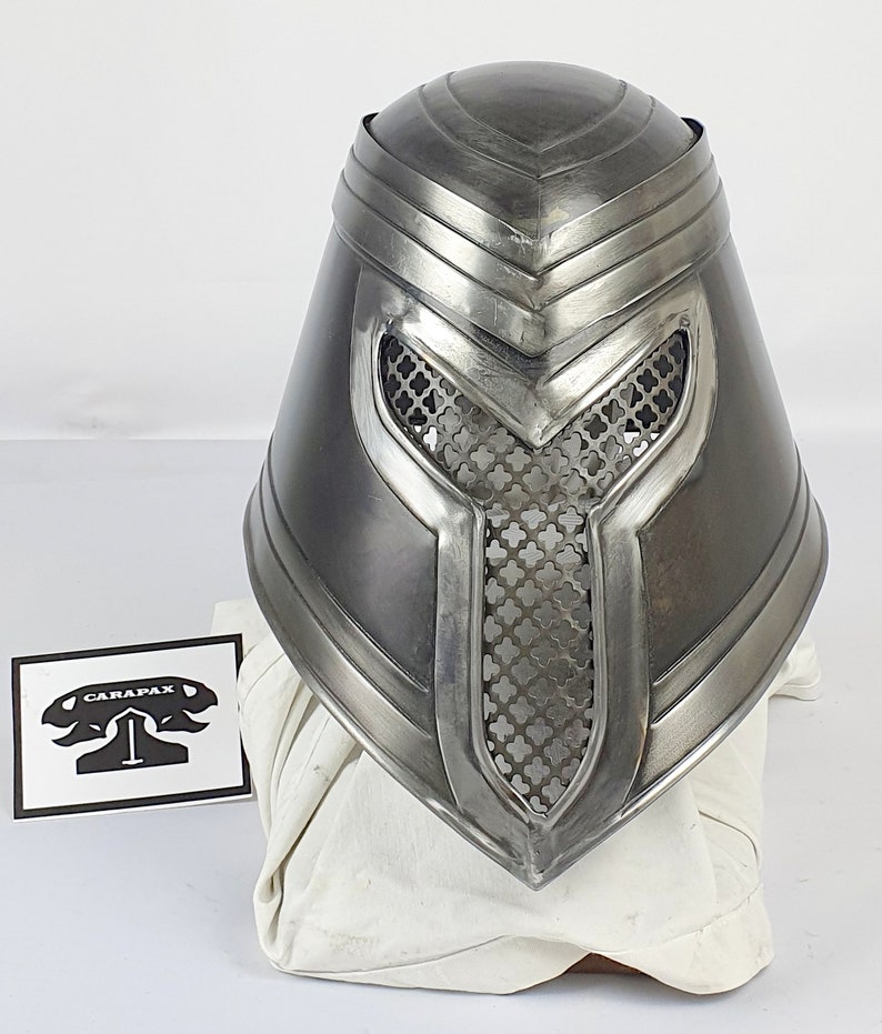 May include: A silver helmet with a mesh faceplate and a pointed top. The helmet has a decorative design on the top and sides.