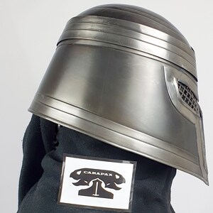 May include: A silver helmet with a black fabric lining and a black and white sticker with the text "CARAPAX" on it.