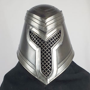 May include: A silver helmet with a mesh face guard and a decorative design. The helmet has a pointed top and a rounded base.