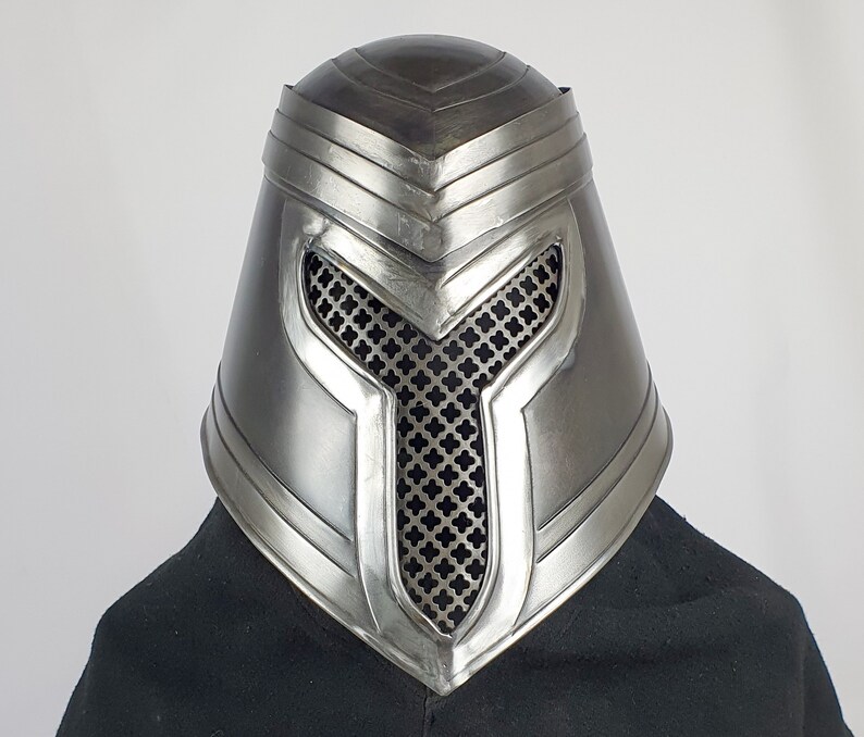May include: A silver helmet with a mesh face guard and a decorative design. The helmet has a pointed top and a rounded base.
