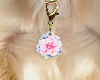 Könnte beinhalten: Ein goldfarbener Hundemarkenanhänger mit einem Aquarell-Design einer rosa und blauen Sukkulentenblüte.