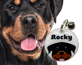 May include: A white round dog tag with a black and brown Rottweiler silhouette and the name "Rocky" printed in black. The tag is attached to a silver chain with a silver bell.