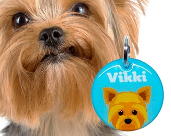 May include: A blue dog tag with a cartoon Yorkshire Terrier and the name "Vikki" printed in white.