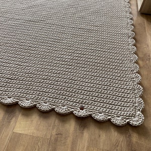 Può includere: Un tappeto beige all'uncinetto con un bordo a festoni. Il tappeto è realizzato con un filato morbido e testurizzato e ha una lucentezza discreta.