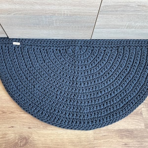 May include: A dark blue crocheted half-circle rug with a textured pattern. The rug is made of thick yarn and has a simple, modern design.