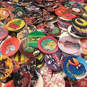 May include: A large collection of colorful plastic game tokens featuring various cartoon characters, logos, and designs. The tokens are round and have a raised edge. Some of the designs include a fly, a basketball player, a cartoon bird, and a skull.