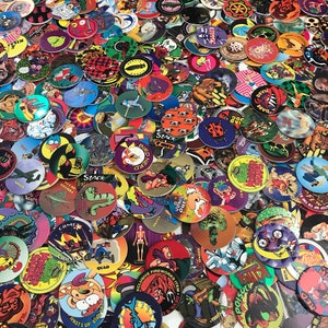 May include: A large collection of colorful, round plastic tokens with various cartoon and graphic designs. The tokens feature characters, animals, and abstract patterns. Some of the tokens have text on them, such as "Stack", "Devil", "Come", "Quad", "What's Up", "Bird", "Zoned Out", "Rhino", "Poison", "Cola", "Creepies", "Cigada", and "Nerd".