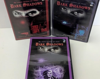 May include: Three black plastic DVD cases for the television series Dark Shadows. Each case features the title in red text, a pair of eyes, and a unique color border: red for Collection 1, blue for Collection 2, and purple for Collection 3.