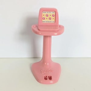 Könnte beinhalten: Ein rosa Barbie-Computerspielzeug. Der Bildschirm zeigt ein Muster aus gelben und rosa Formen. Der Computer steht auf einem Ständer mit einer Tastatur und dem Barbie-Logo an der Basis. Der Bildschirm zeigt die Website-Adresse www.barbie.com.