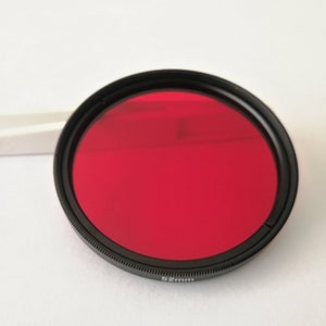 Puede incluir: Un filtro rojo para cámara con un borde negro y un diámetro de 52 mm.