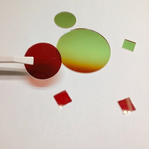 May include: Assortment of red and green glass filters in various shapes and sizes, including circles and squares. The filters are arranged on a white surface.