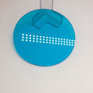 Könnte beinhalten: Eine runde, leuchtend blaue Glasscheibe mit einem transparenten Eckständer aus Kunststoff. Die Scheibe hat ein dezentes, gepunktetes Muster.