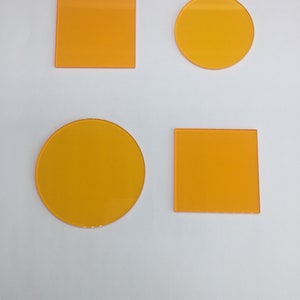 May include: Four orange-colored geometric shapes: two squares and two circles. The shapes are made of a translucent material and are arranged in a grid pattern.