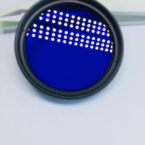 May include: A blue camera lens filter with a black rim and a pattern of small white dots.