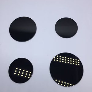 Puede incluir: Cuatro discos redondos negros de diferentes tamaños. Los dos discos más grandes son de color negro sólido, mientras que los dos discos más pequeños tienen un patrón de pequeños puntos blancos.