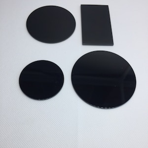 May include: Four black circles and a black rectangle, all made of a smooth, glossy material. The circles are of varying sizes, and the rectangle is slightly larger than the smallest circle.
