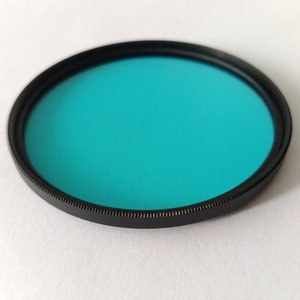 May include: A round, black-rimmed filter with a bright turquoise blue glass lens.