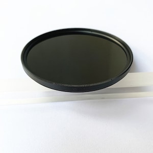 May include: A black camera lens filter with a textured rim.