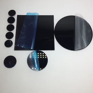 May include: A set of black circular adhesive backed mirror tiles. The set includes a large round mirror tile, a smaller round mirror tile, and a square mirror tile. The tiles are all covered with a protective film.