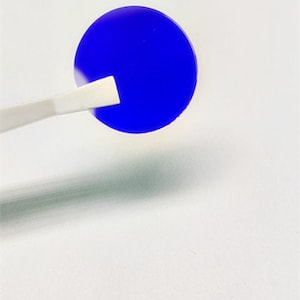 Puede incluir: Un disco redondo azul sostenido por pinzas. El disco es un filtro para un microscopio.