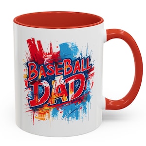May include: White ceramic mug with a red interior and handle. The mug features the text "BASEBALL DAD" in red and blue, with a baseball graphic, set against a colorful splatter design.