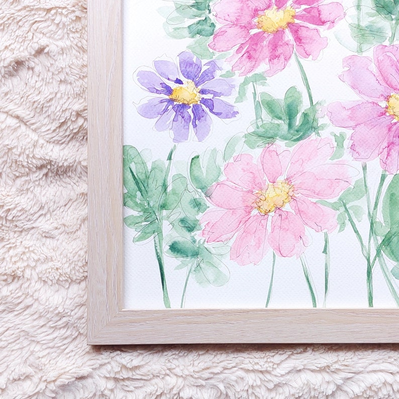 Pode incluir: Pintura em aquarela de flores rosa e roxas com centros amarelos e folhas verdes. A obra de arte &eacute; emoldurada em uma moldura de madeira de cor clara. A pintura tem um estilo suave e delicado.