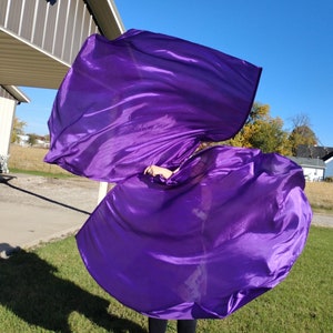 May include: A person is holding and twirling a large purple fabric, creating a flowing, dynamic shape. The fabric is silky and has a slight sheen. The person is wearing black pants and shoes.