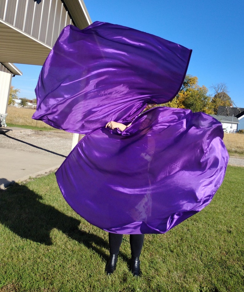 May include: A person is holding and twirling a large purple fabric, creating a flowing, dynamic shape. The fabric is silky and has a slight sheen. The person is wearing black pants and shoes.