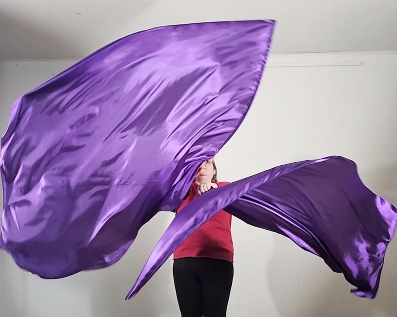 May include: A person is holding two purple satin dance flags. The flags are flowing in the air.
