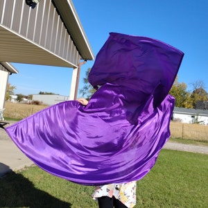 May include: A person is holding a large purple fabric flag, flowing in the wind. The flag is made of a silky material and has a smooth, flowing texture.