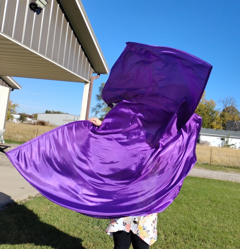 May include: A person is holding a large purple fabric flag, flowing in the wind. The flag is made of a silky material and has a smooth, flowing texture.